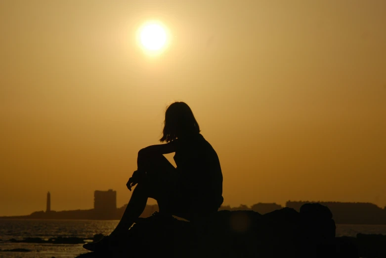 a woman sitting on top of a rock near the ocean