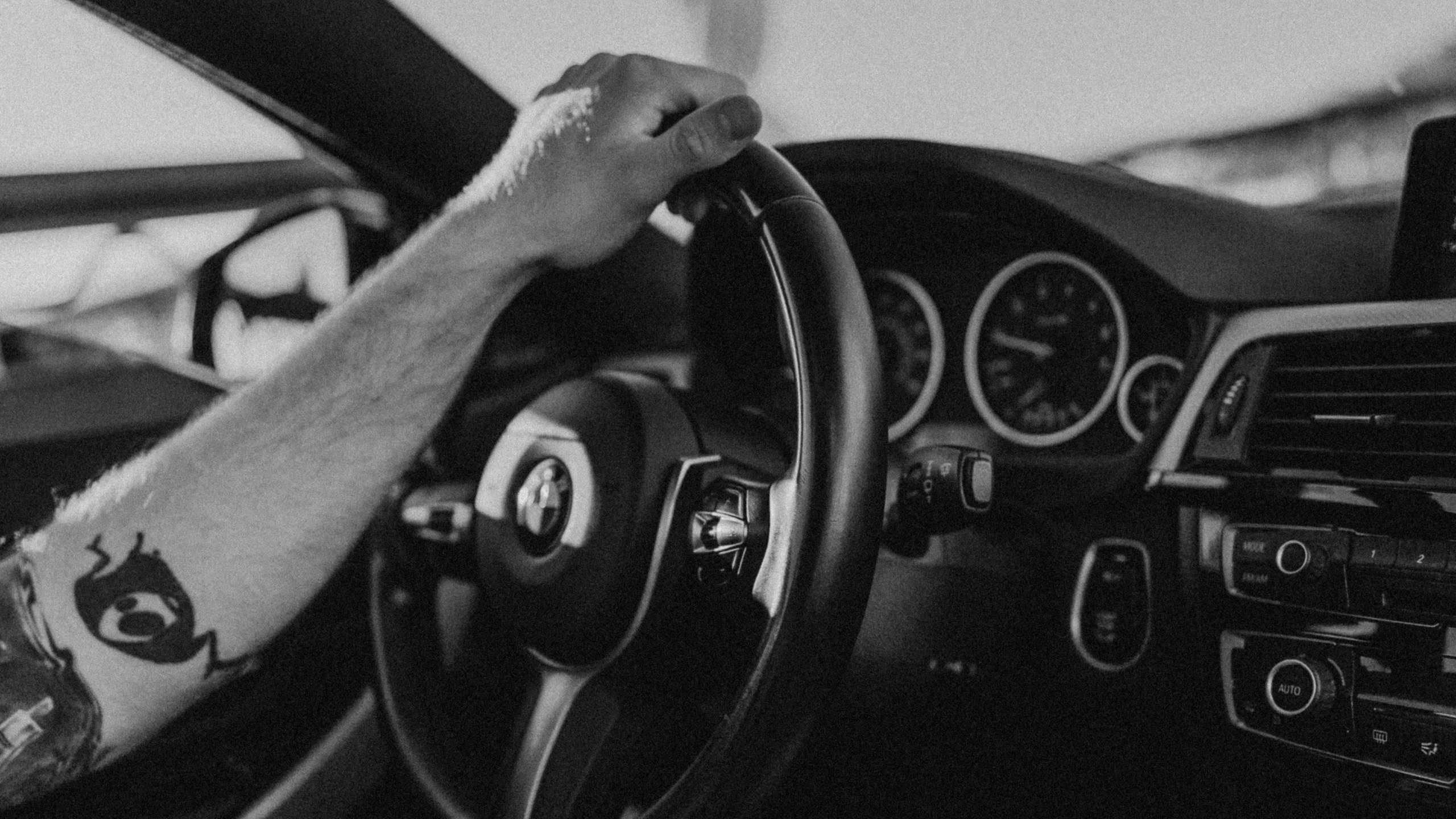 the inside view of a black and white po shows hands on the wheel of an older model car