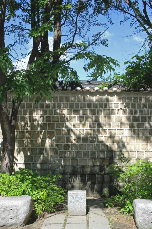 a brick wall near two cement planters and trees