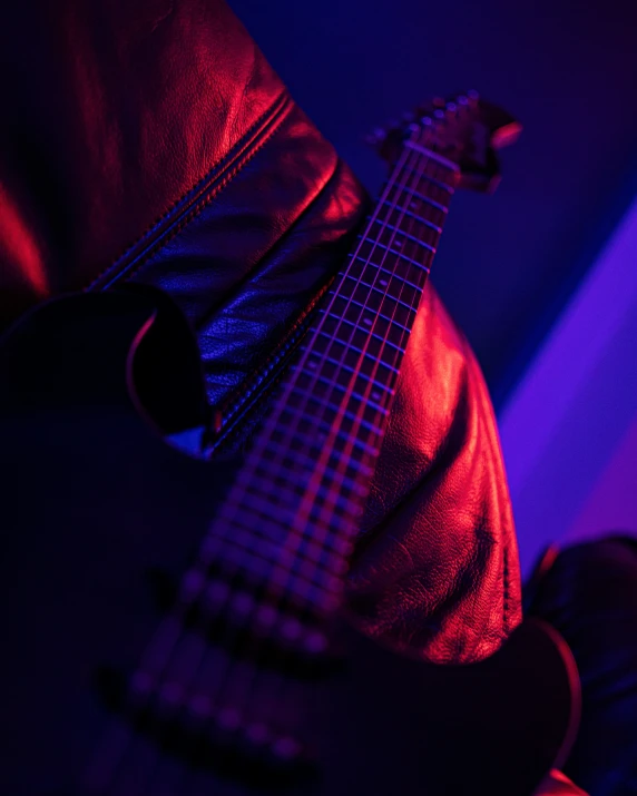 a person's hand holding a guitar in purple and red light