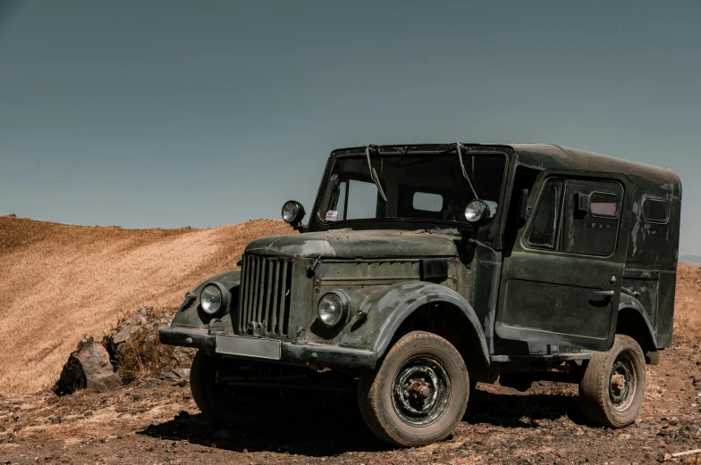 an old green truck parked in the middle of the desert