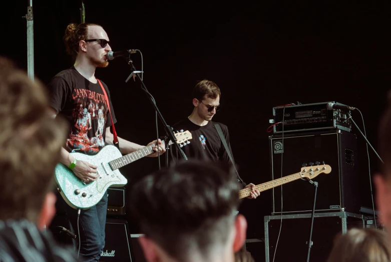 two guys playing instruments in a band while a girl sits