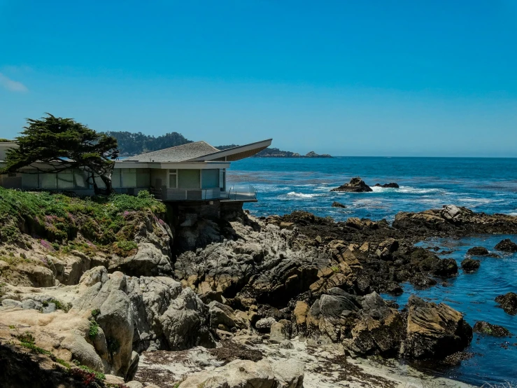 a small house that is on the edge of a cliff by some water