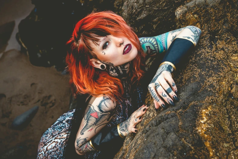 a girl with red hair wearing tattoos leaning on a rock