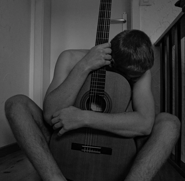 a man sitting with his arms around an acoustic guitar