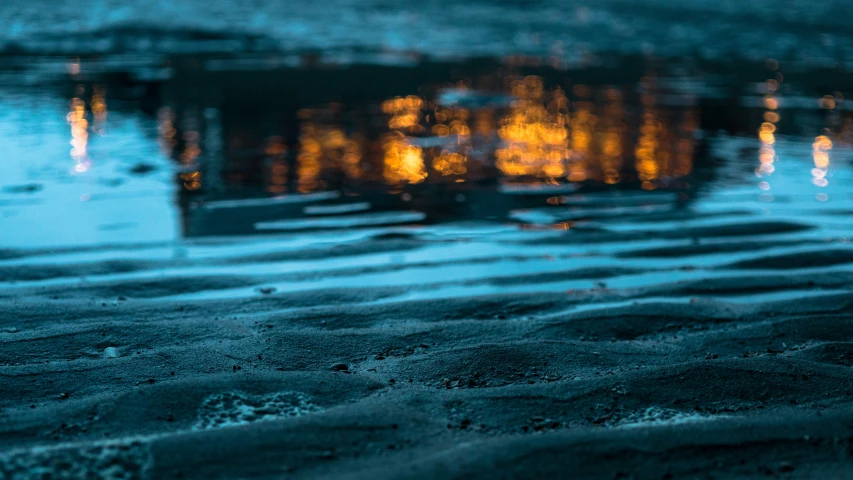 water on the ground in front of a building with lights reflecting off of it