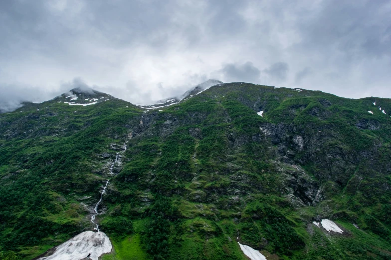 a green mountain side has a cloudy sky