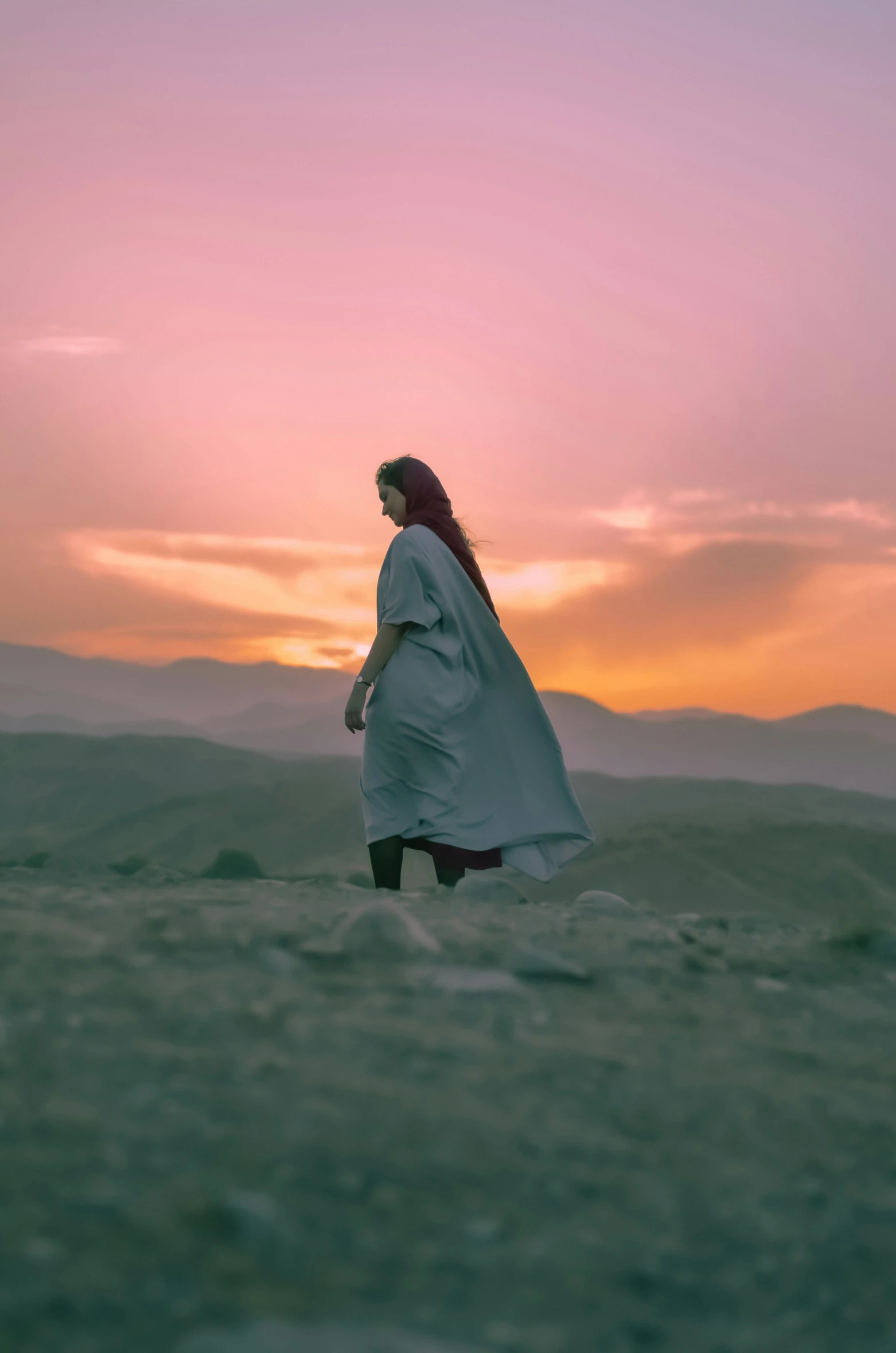 the woman is walking through a barren area at sunset