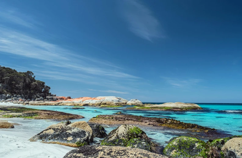 some rocks and clear blue water near a sandy shore