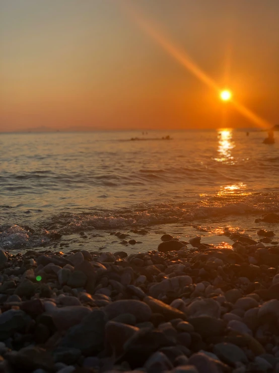 a sunset shines in the distance over a rocky beach