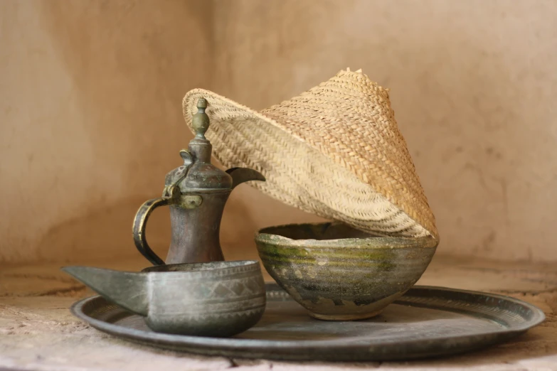 straw hat on a metal tray next to an old fashioned tea kettle