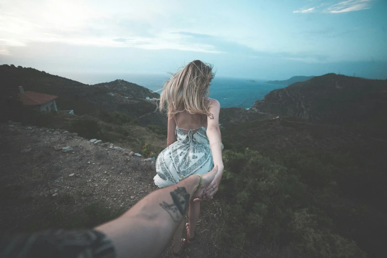 a woman sitting on the edge of a cliff holding the arm of a man