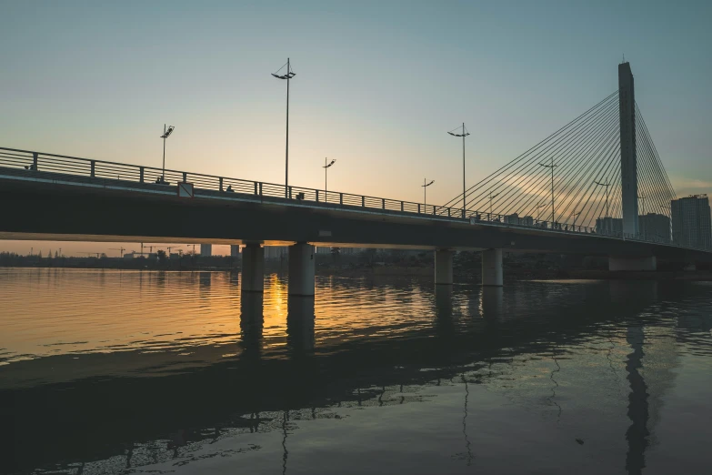 a sun sets on a bridge over the water with the bridge going through