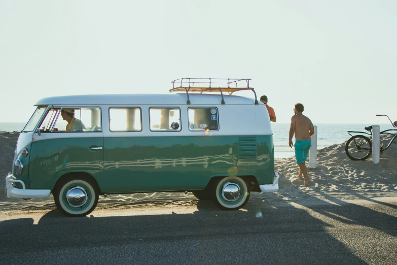 two men stand by an old van on the beach