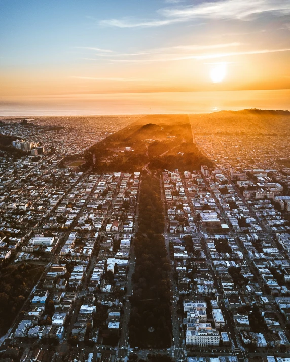 the sun sets over a city and hills