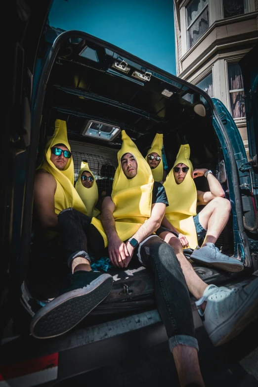 four men dressed up like banana suits sit inside a van