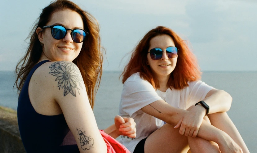 two women sitting down on a beach posing for a picture