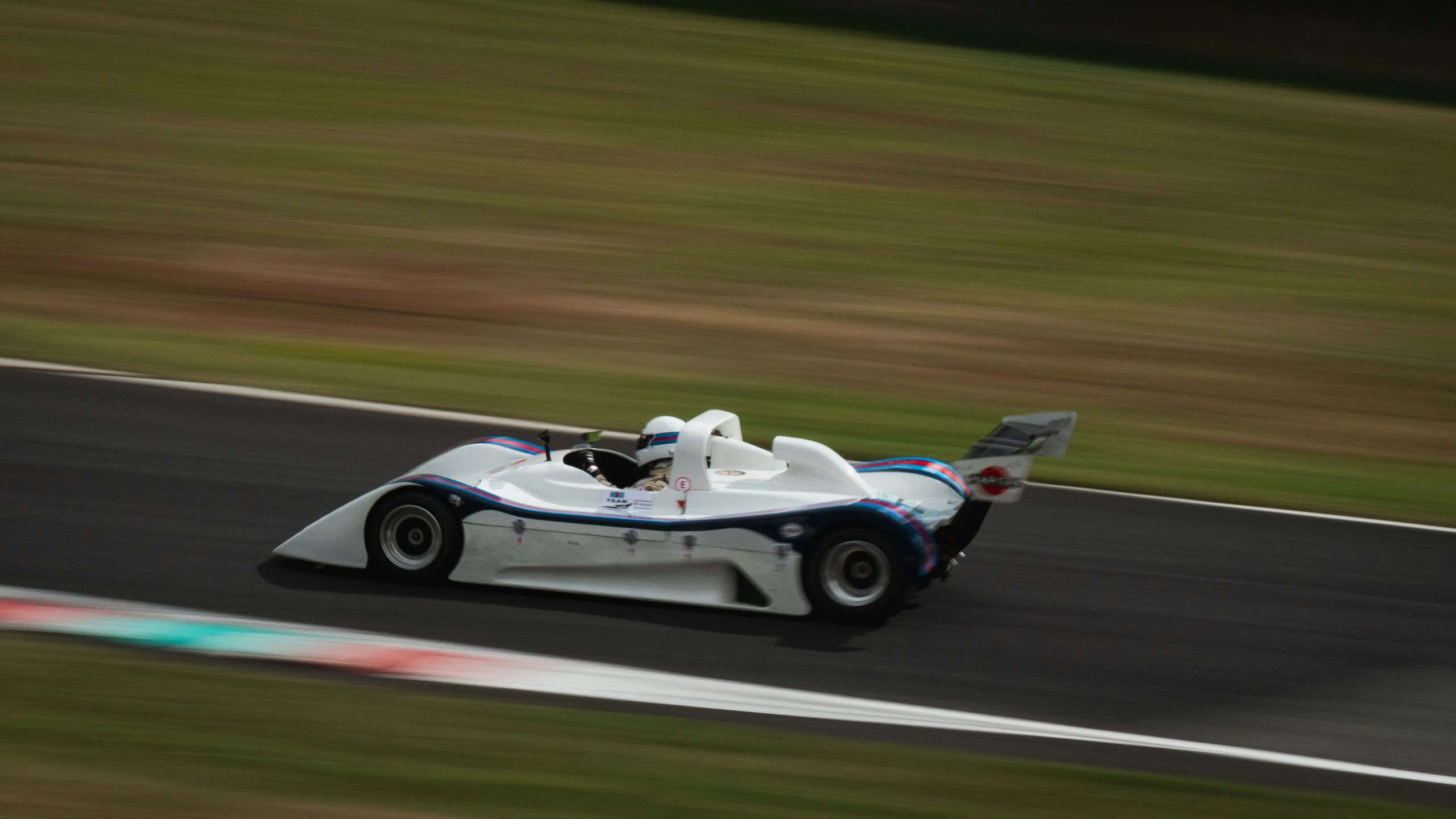 a white car driving on the racetrack with grass in the background