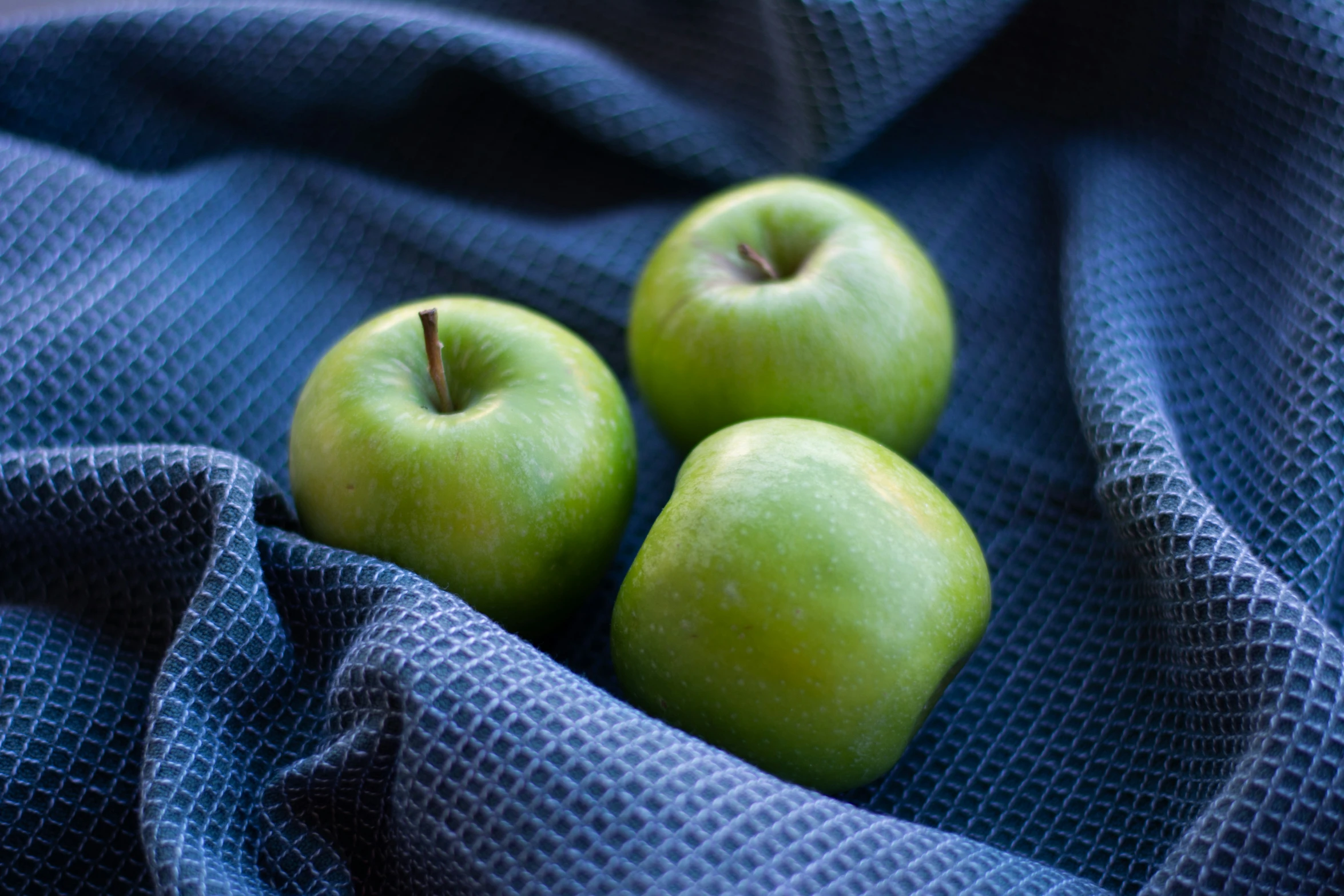 a couple of green apples sitting on top of a blue cloth