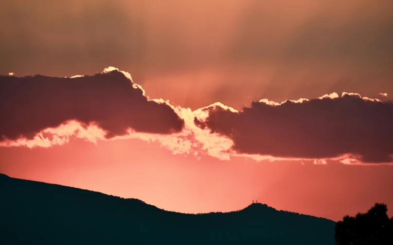 the sun is setting behind a mountain and it has lots of clouds