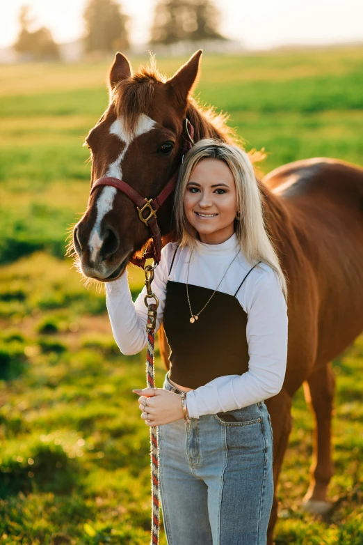 girl in jeans and overalls poses with a brown horse