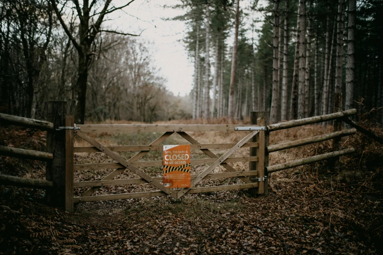 a wooden fence in the woods with a sign stating a closed gate