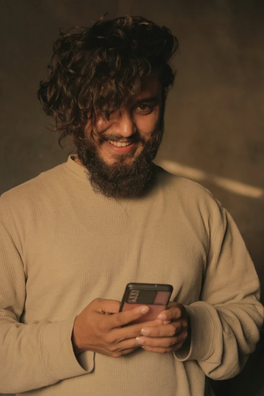 a bearded man wearing a brown sweater holding his cell phone