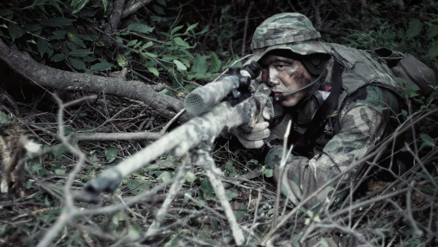 a man in camouflage crouches in the brush with a rifle