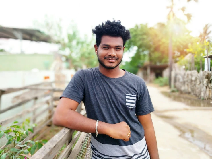 a man leaning against a fence smiling and looking at the camera