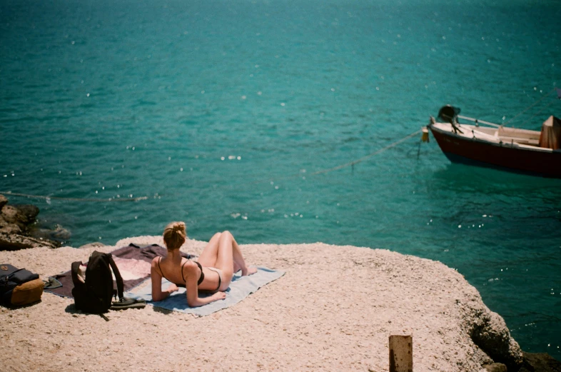 a girl laying on a towel on top of sand near water