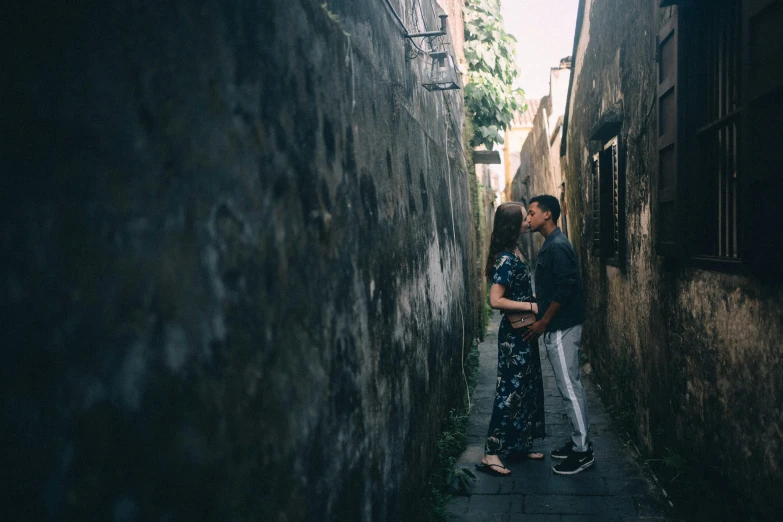 two people are kissing next to each other in the narrow alleyway