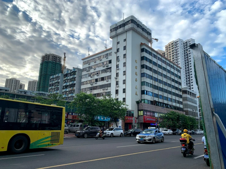 a city street with cars, motorcycle and large building in the background