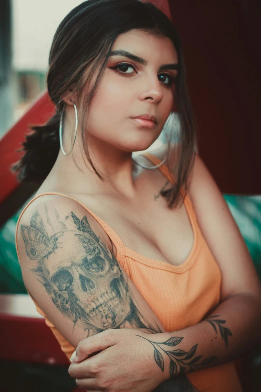 girl in orange tank top with large tattoos leaning up