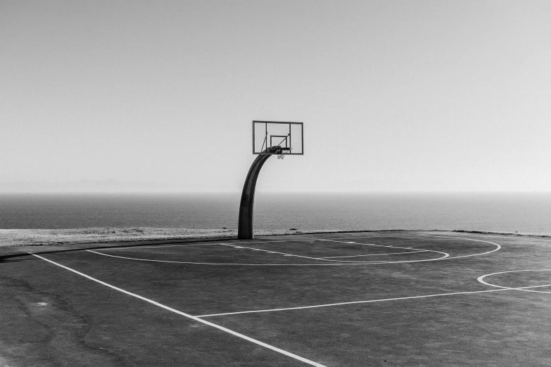 an asphalt basketball court next to the ocean