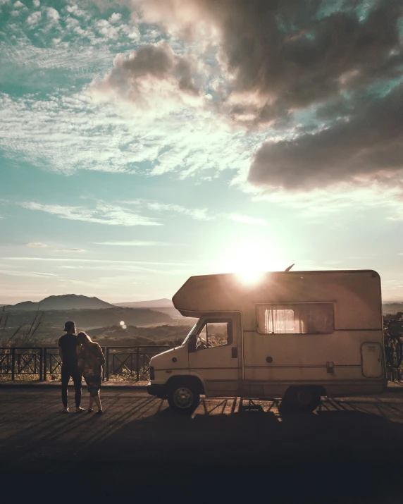 two people stand outside of an rv parked in front of mountains