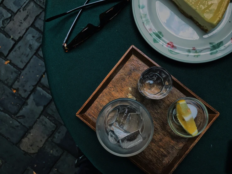 a wooden tray filled with glasses of water next to a slice of lemon cake