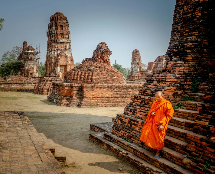 a person in orange robe on steps in front of pagodas