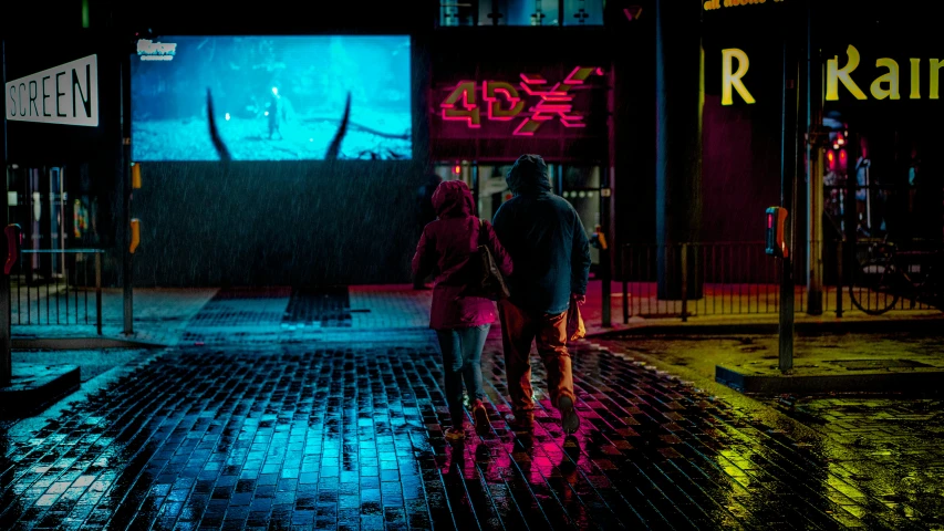 two people standing outside with a neon blue building behind them