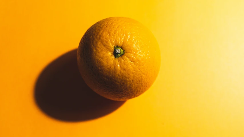 an orange is sitting against a yellow wall