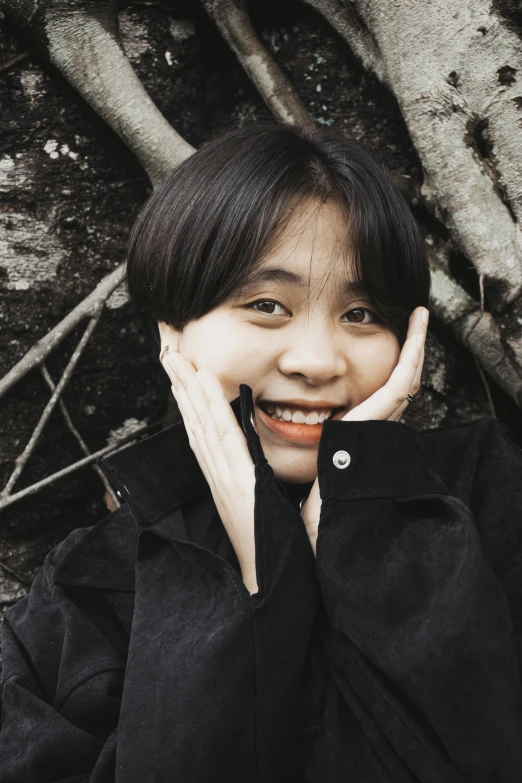 a young asian woman poses for the camera in front of an old tree