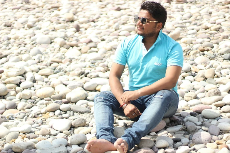 man with eyeglasses sitting on a rocky beach