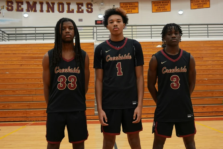 three s are standing in the middle of an indoor basketball court