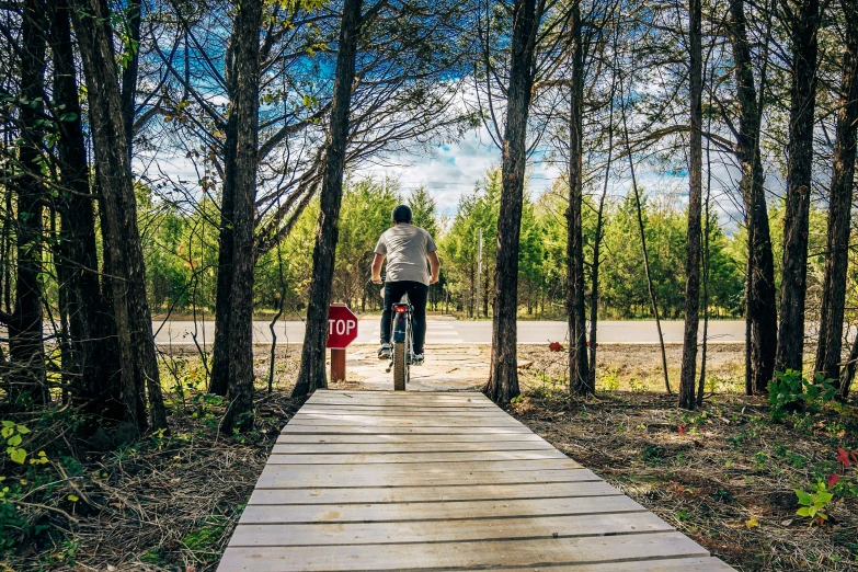 a man riding his bike down a sidewalk in the middle of a forest