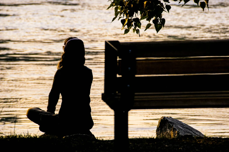 a woman sitting in front of a bench next to the water