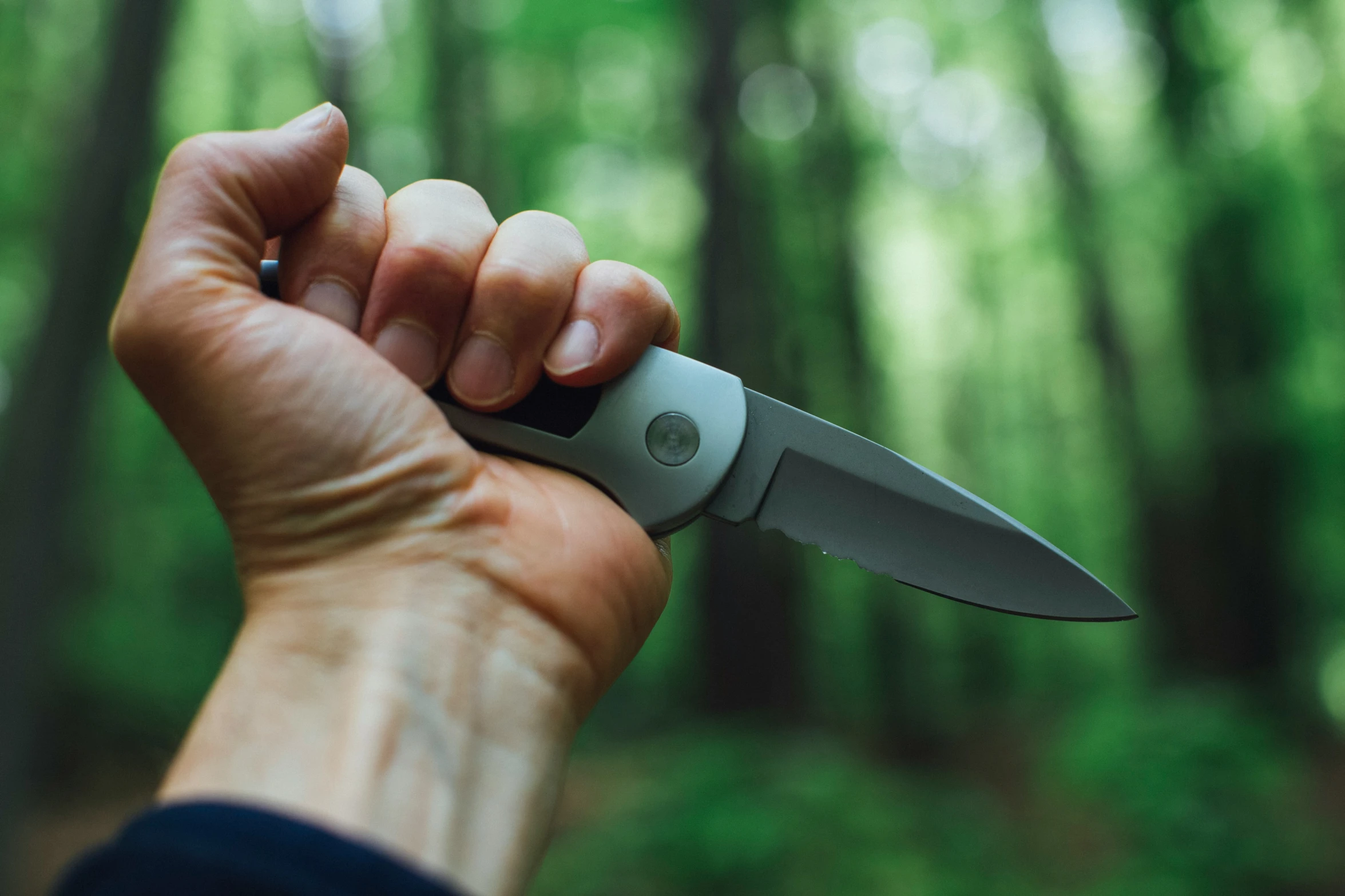 a hand holding a knife near the woods