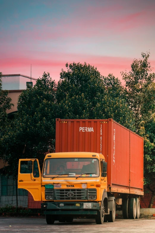 two orange trucks parked near one another near the trees