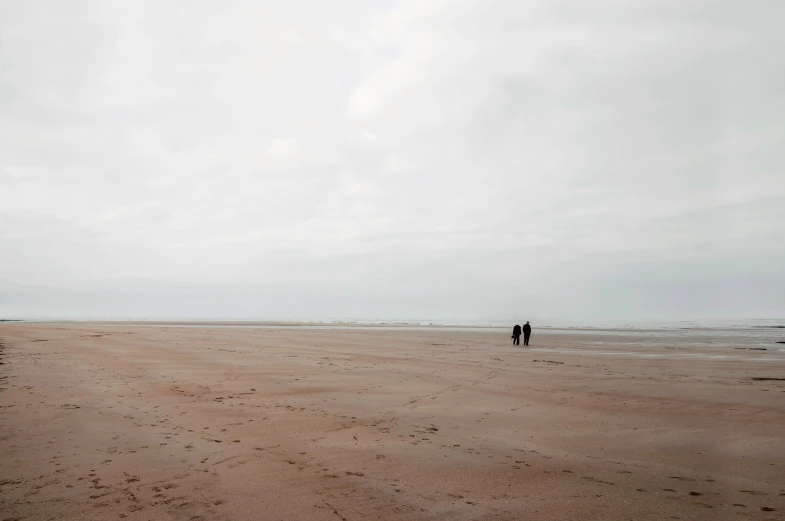 two people standing on a sandy beach near water