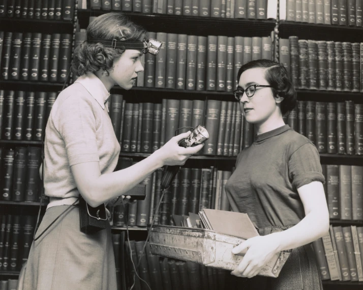 two women standing near one another in front of a bookshelf
