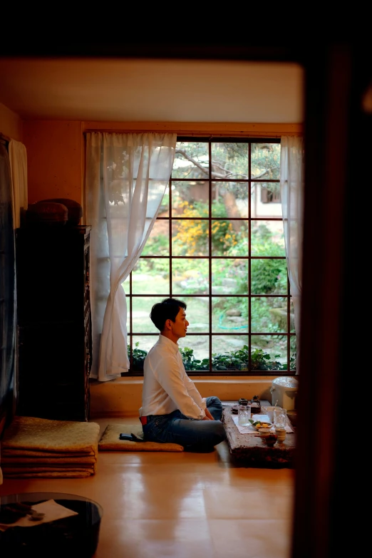 a man sitting in front of a window on top of a hard wood floor