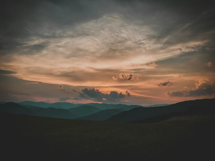 some hills and mountains under a cloudy sky